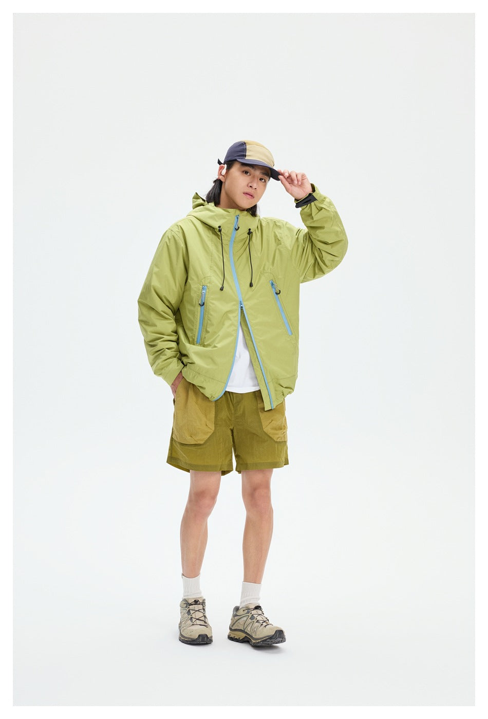 Front view of a model wearing a lime-green hooded jacket with blue zippers and olive shorts.