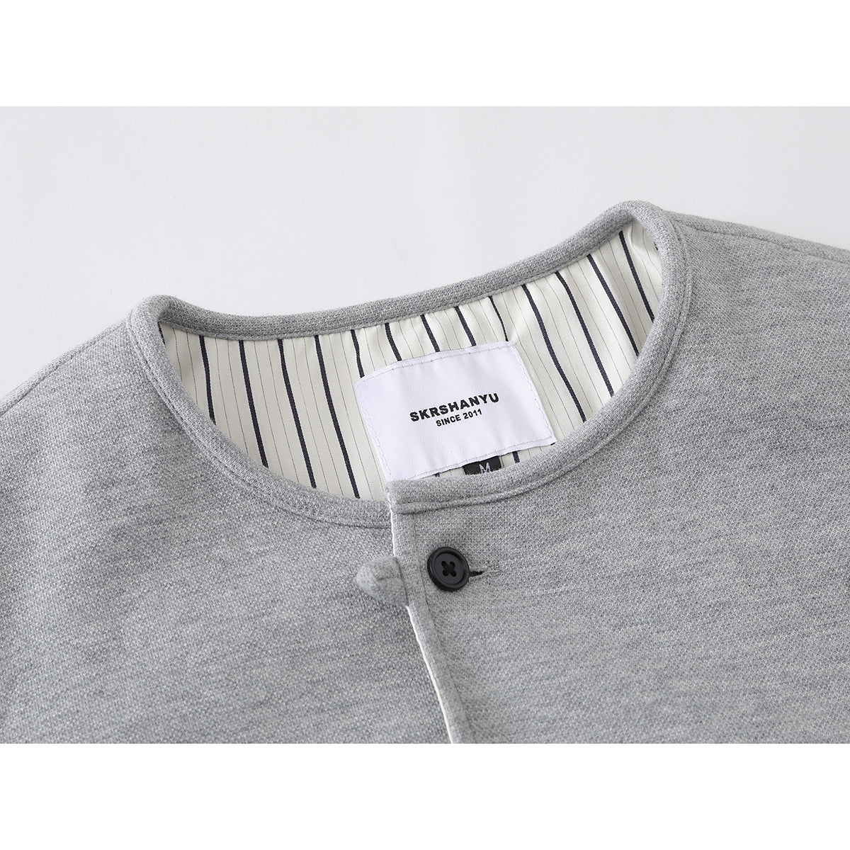 Close-up of a light gray jacket collar, striped inner lining, black button, and sewn-in neck label.