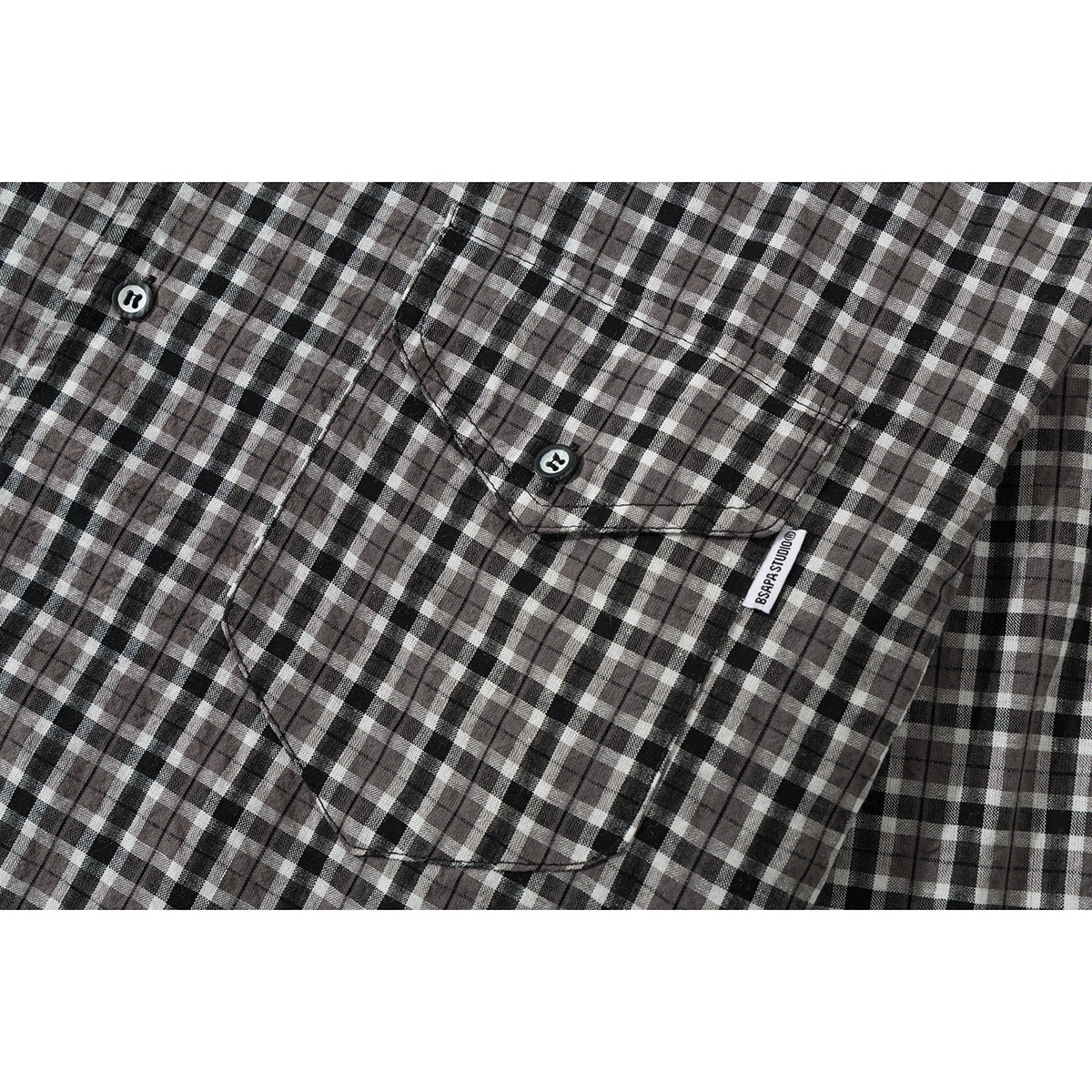 Close-up of a black, gray, and white plaid shirt showing a buttoned chest pocket and small fabric label.