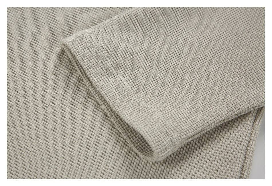 Close-up of a light beige-gray garment showing its small waffle-like knit texture and folded edge.
