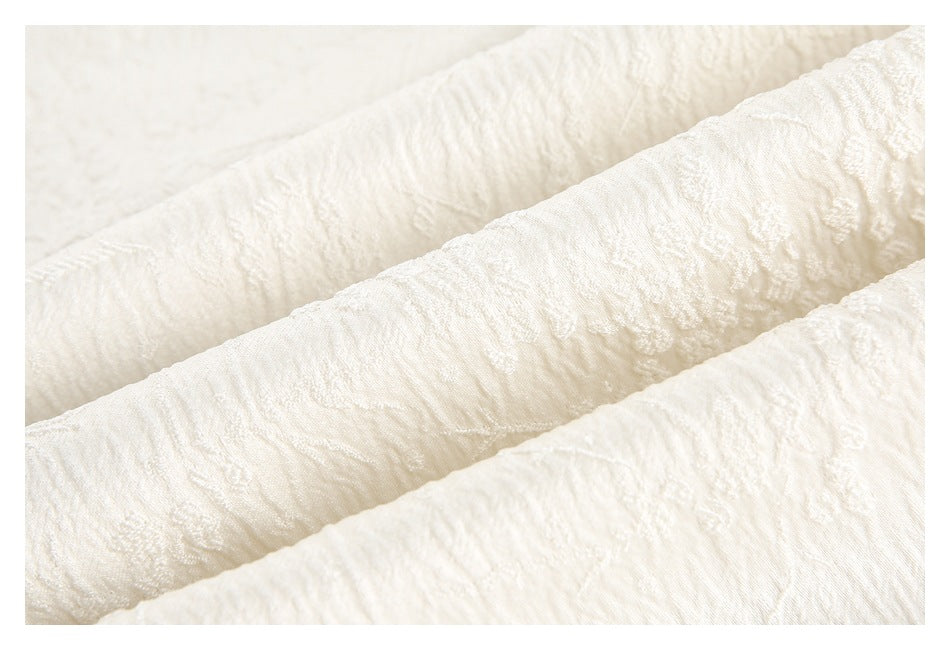 Close-up of ivory textured fabric arranged in soft folds, highlighting its raised floral pattern.