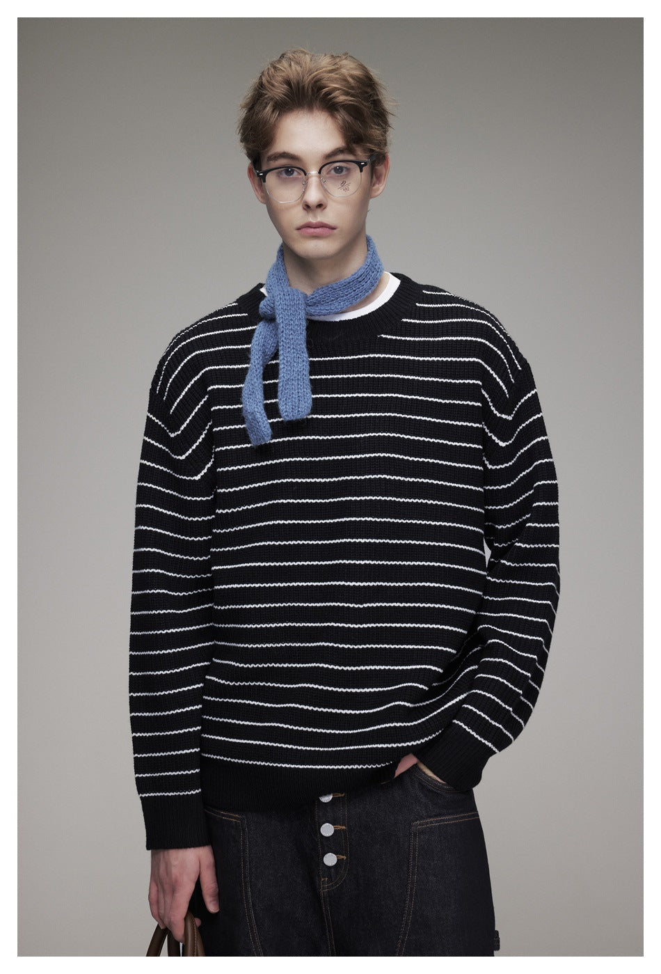 Closer view of a model wearing a black sweater with white horizontal stripes and a blue scarf.