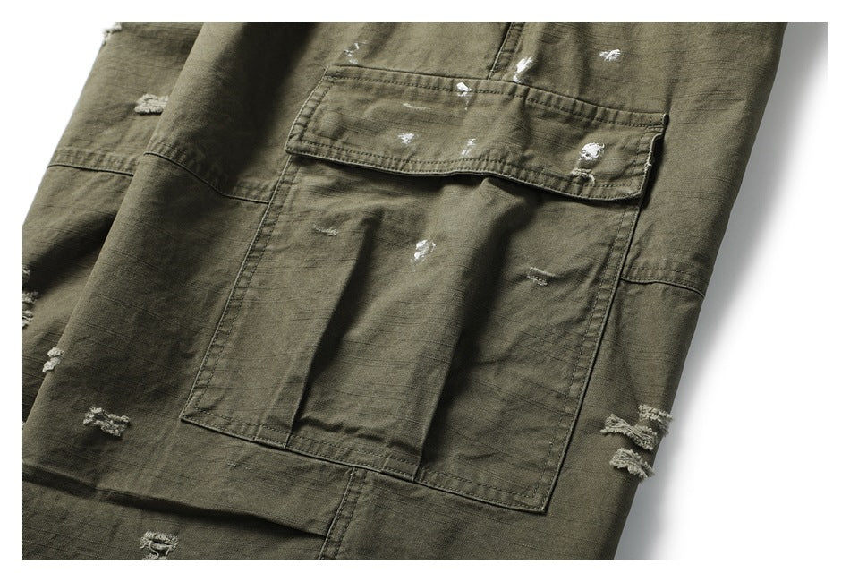 Close-up of an olive drab garment with a large flap pocket, stitched panels, and scattered distressed white abrasions.
