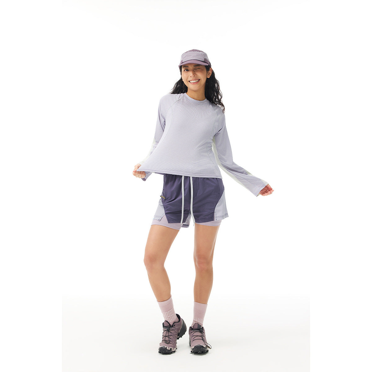 Full-length view of a woman in a pale lavender long-sleeve top with light contrasting sleeves and matching athletic shorts.