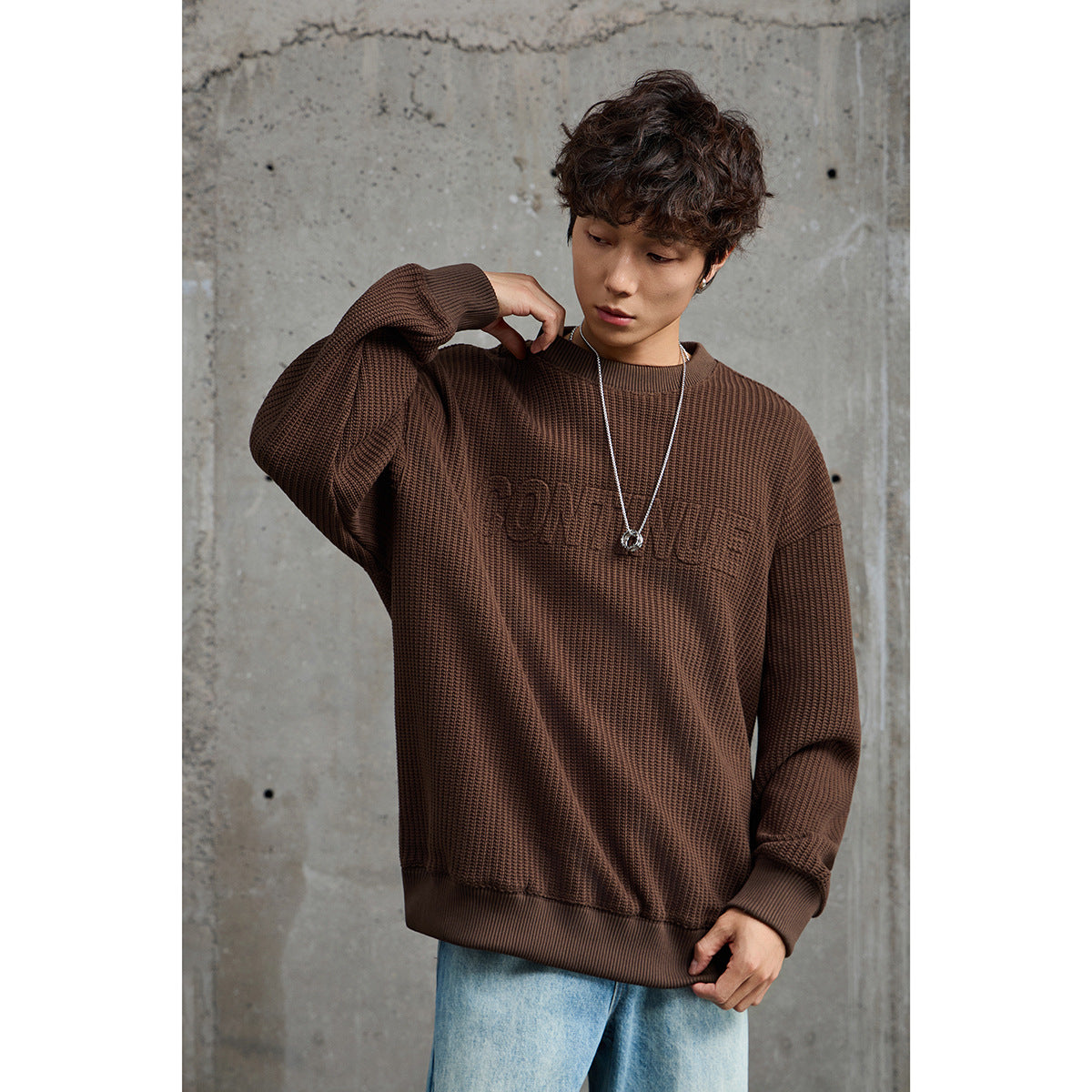 Model wearing a brown textured crewneck sweater with ribbed trim and light blue jeans.