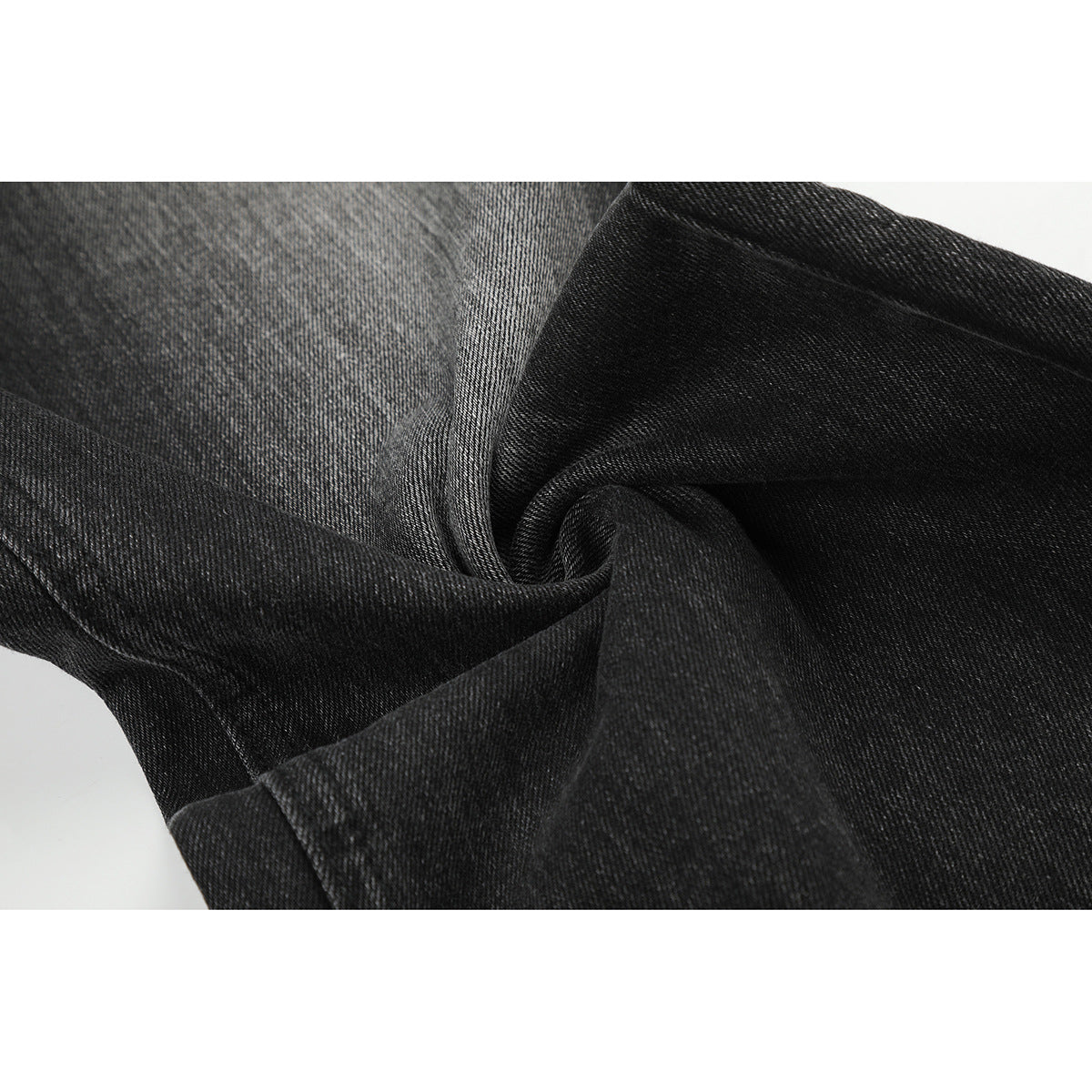 Close-up of charcoal-black denim folded to show its diagonal weave and surface texture.