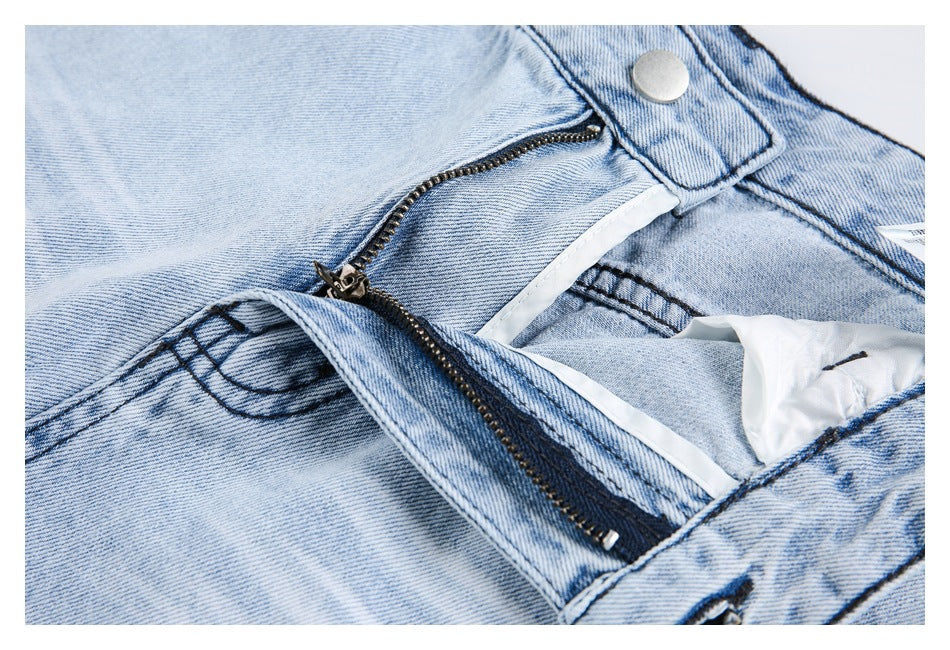 Close-up of light-wash jeans with the front zipper open, showing the fly and waistband button.