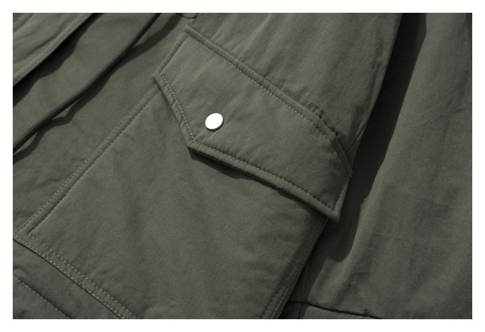 Close-up of an olive jacket's large flap pocket with a silver snap button and topstitching.