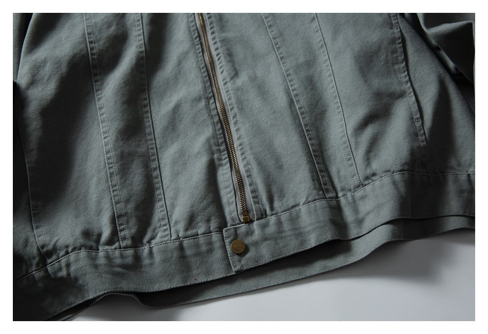 Close-up of the gray-green jacket's lower front, showing vertical seams, a brass-colored zipper, and a buttoned hem tab.