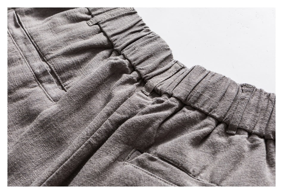 Close-up of gray trousers showing a gathered elastic waistband, stitching, and part of a pocket.