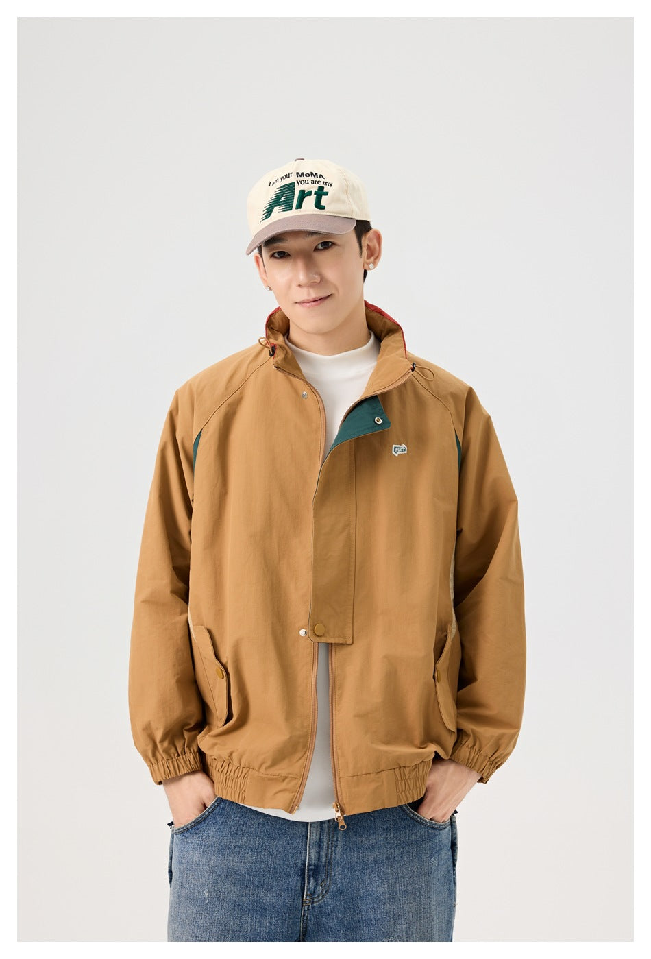 Close front view of a model wearing a tan jacket with dark teal accents, snap flap and zip closure.