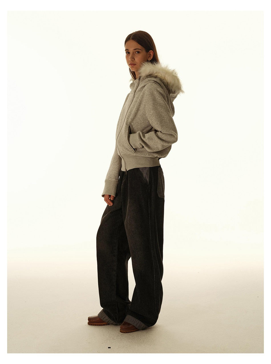 Three-quarter side view of a model in a gray zip hoodie with white fur hood trim and wide black pants.