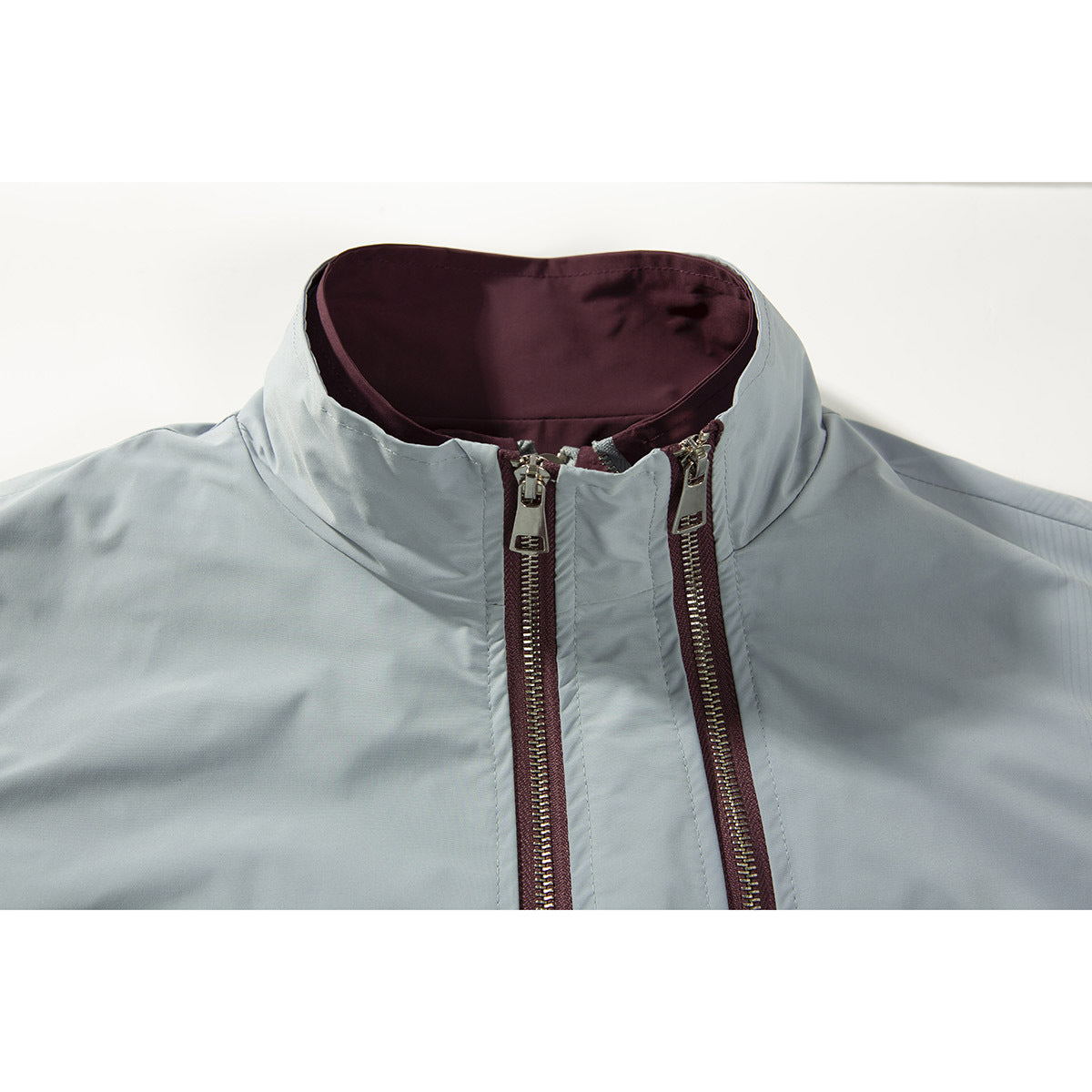 Close-up of a pale blue-gray jacket's high collar and paired burgundy-trimmed front zippers.