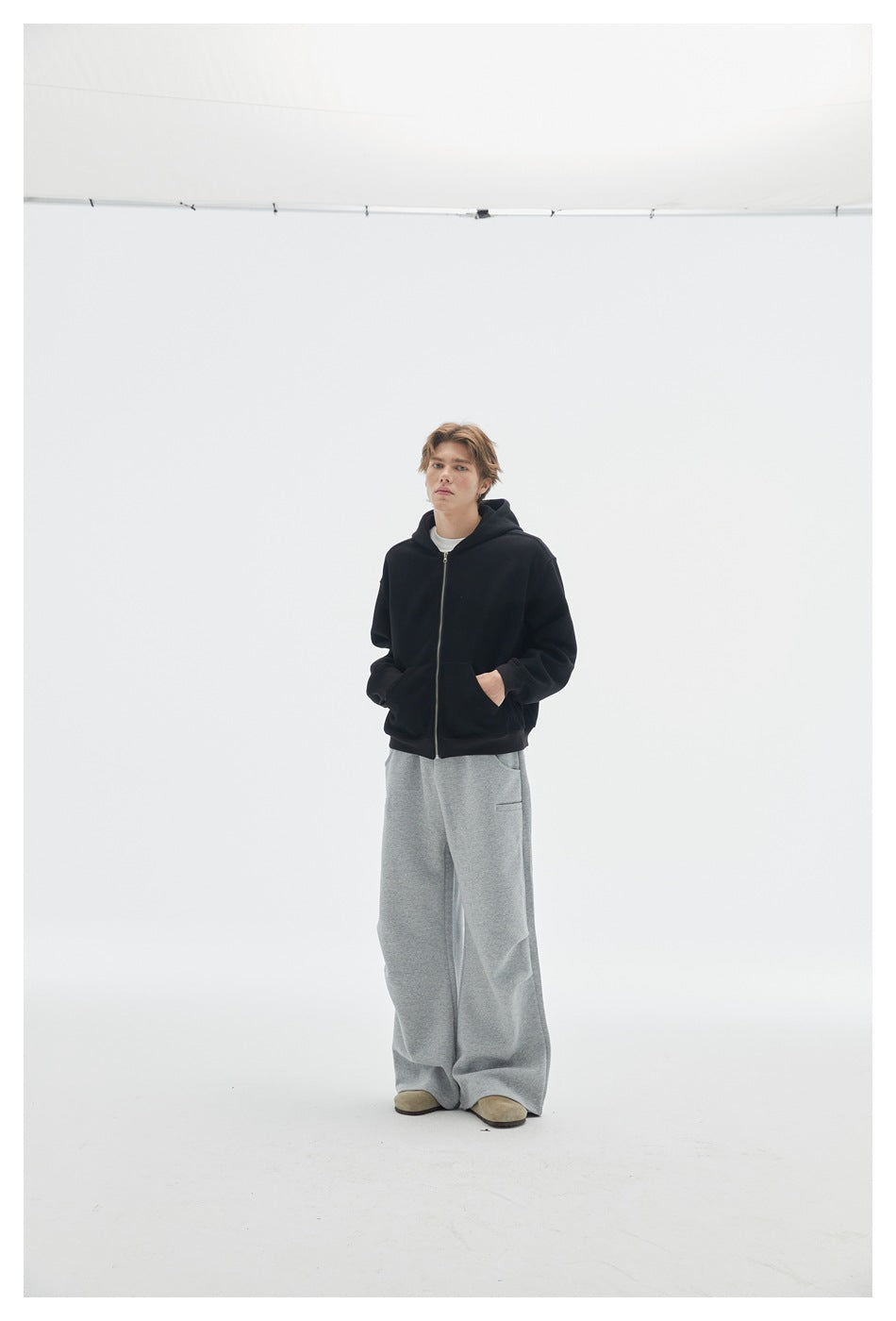 Front view of a model in a black zip-up hoodie and loose gray sweatpants.