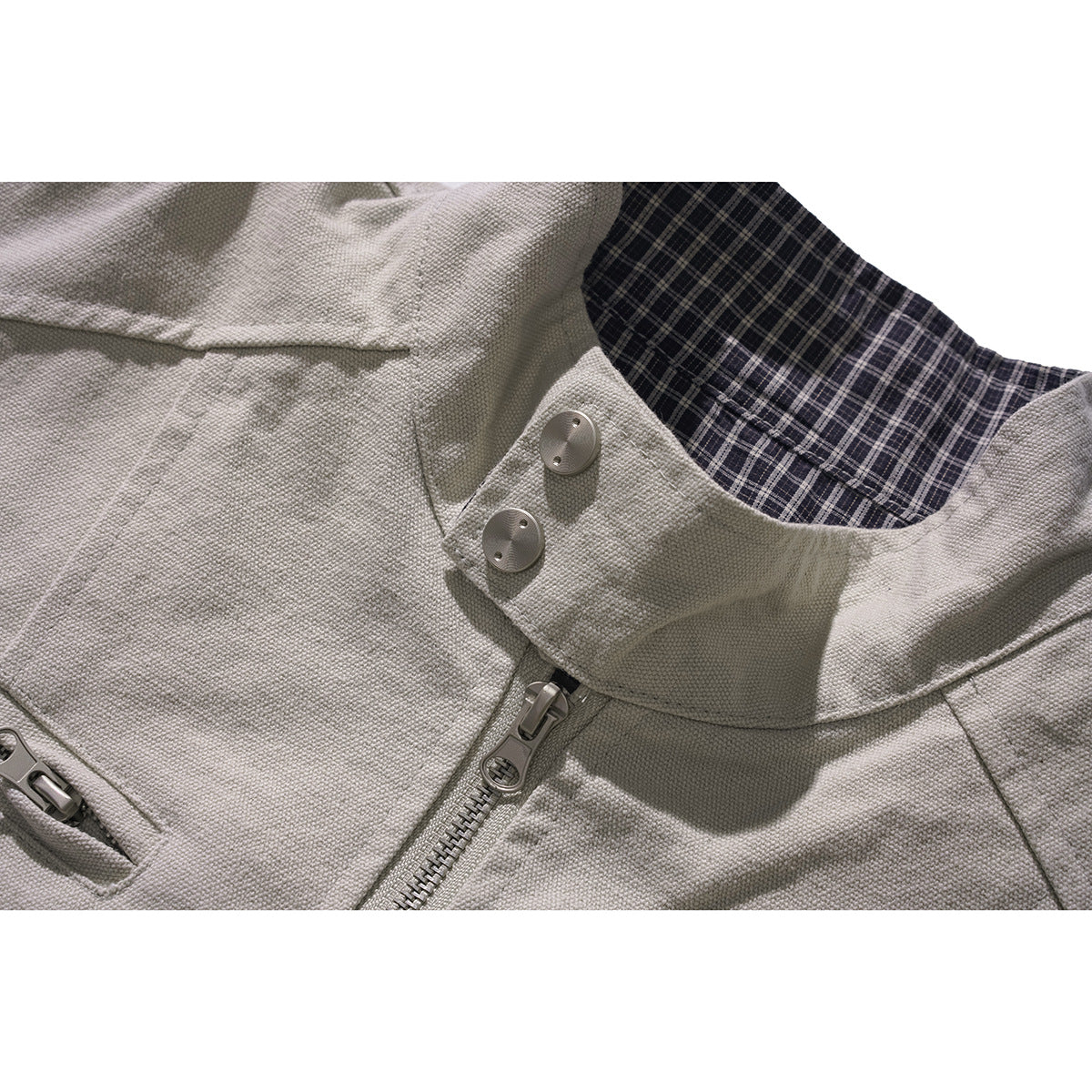 Close-up of a light gray jacket collar with dark plaid lining, two buttons, and a front zipper.