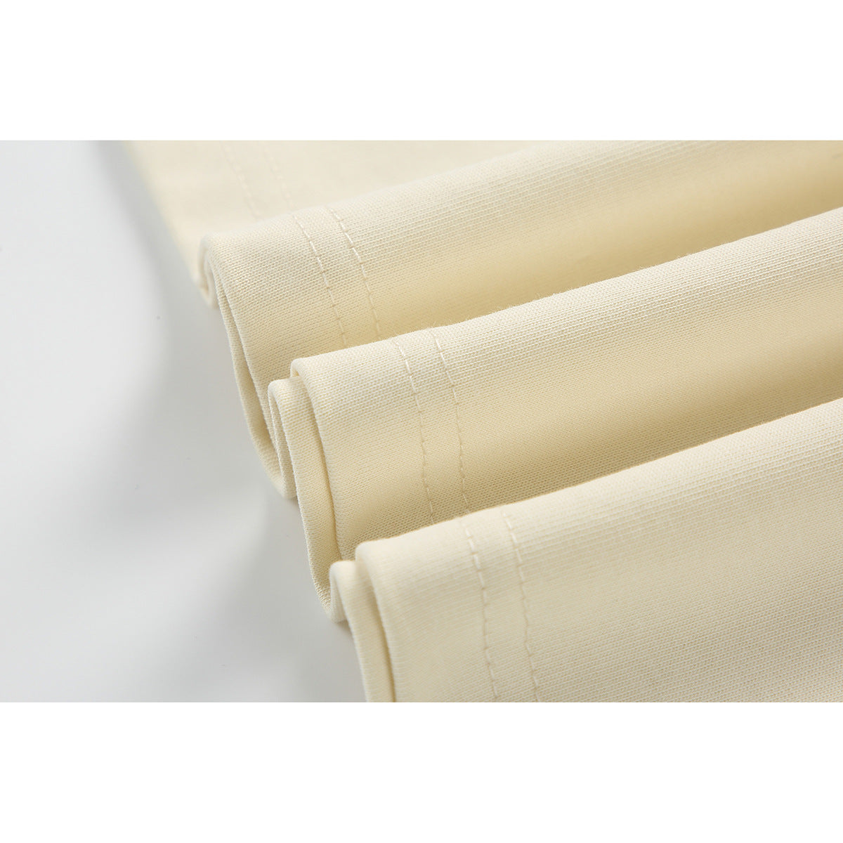 Close-up of several folded cream garment hems, each with parallel rows of stitching.