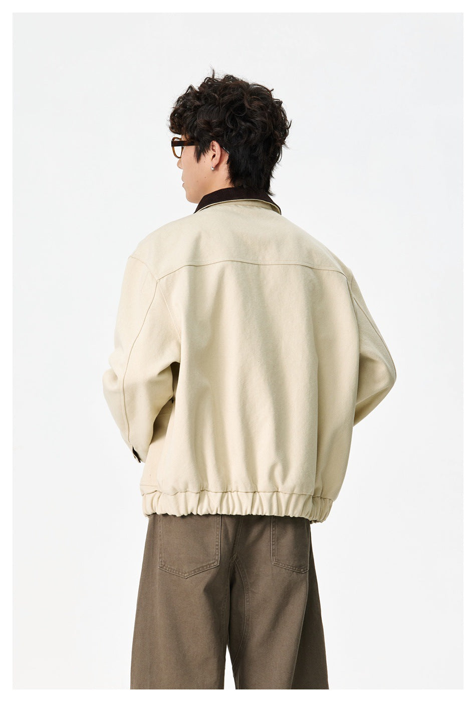 Rear view of a model wearing a cream jacket with a dark brown collar and gathered hem.