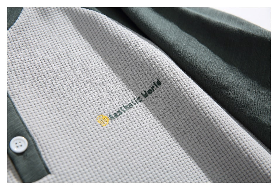 Close-up of dark green lettering and a small yellow emblem embroidered on the light gray waffle-knit shirt.