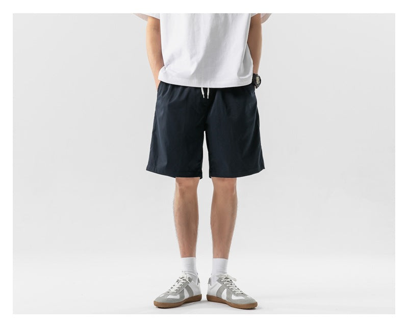 Model wearing navy drawstring shorts with a white T-shirt and white sneakers, front view