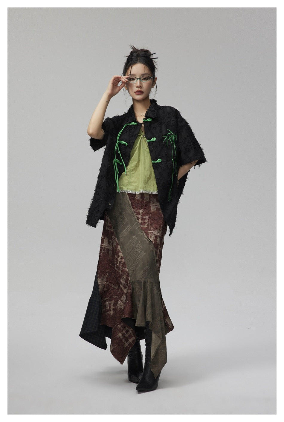 Model in black textured short-sleeve shirt with green knot closures and bamboo embroidery, hand raised to glasses