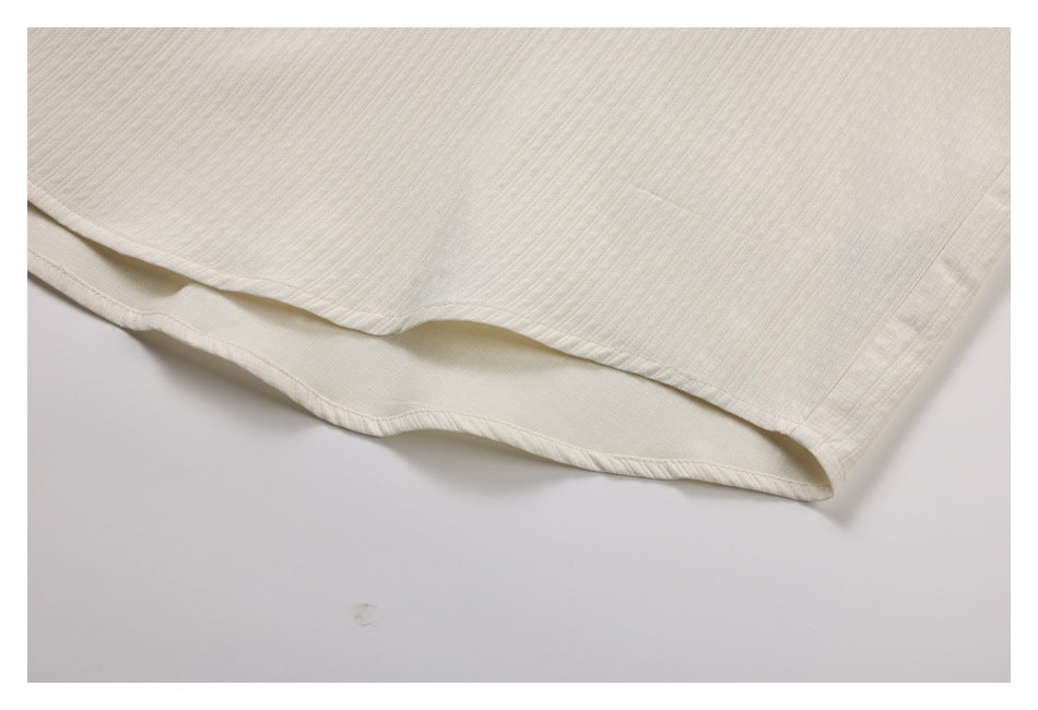 Close-up of the ivory shirt's curved hem and stitched edge, showing its ribbed texture.