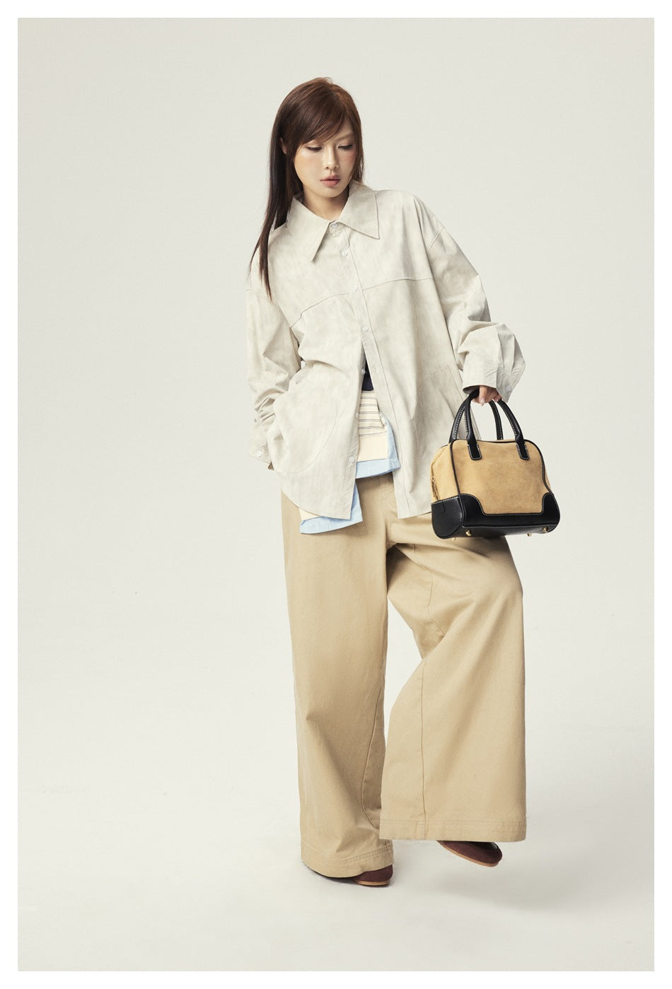 Model wearing an oversized ivory button-up jacket with large patch pockets and wide-leg tan trousers, carrying a