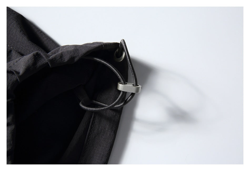 Close-up of a black cord loop and metal eyelet at the edge of charcoal pants.