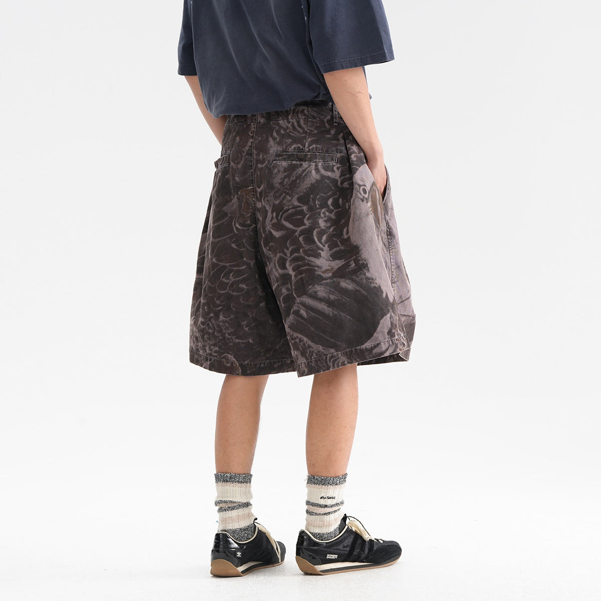 Back view of a model wearing loose charcoal-gray printed shorts with an elastic waistband and back welt pockets.