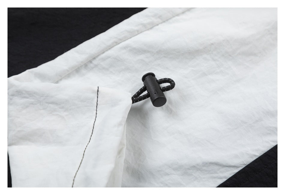 Close-up of a black cord toggle against a white garment panel.