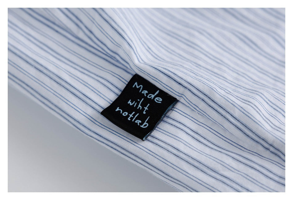 Close-up of a black sewn label with white lettering on white fabric with fine blue stripes.