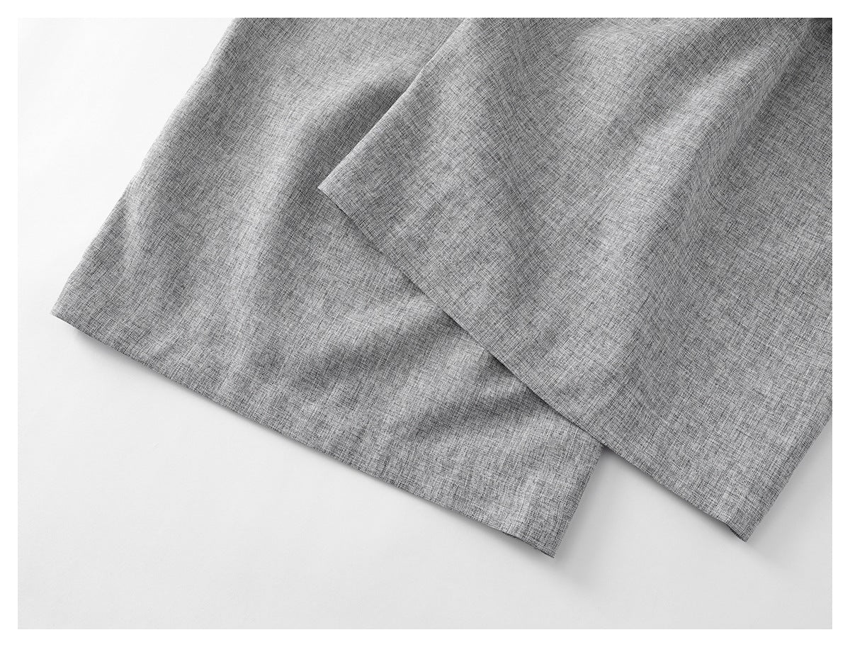 Close-up of the hems of light gray textured trouser legs.