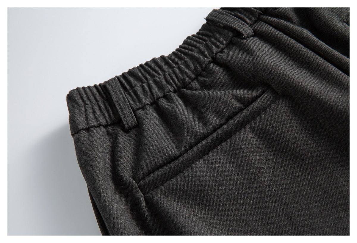 Close-up of dark charcoal trousers showing the gathered elastic waistband and slanted front pocket.