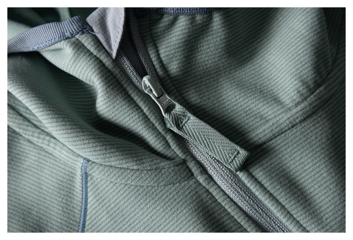 Close-up of a sage-green jacket zipper, ribbed fabric, and gray-blue seam trim.
