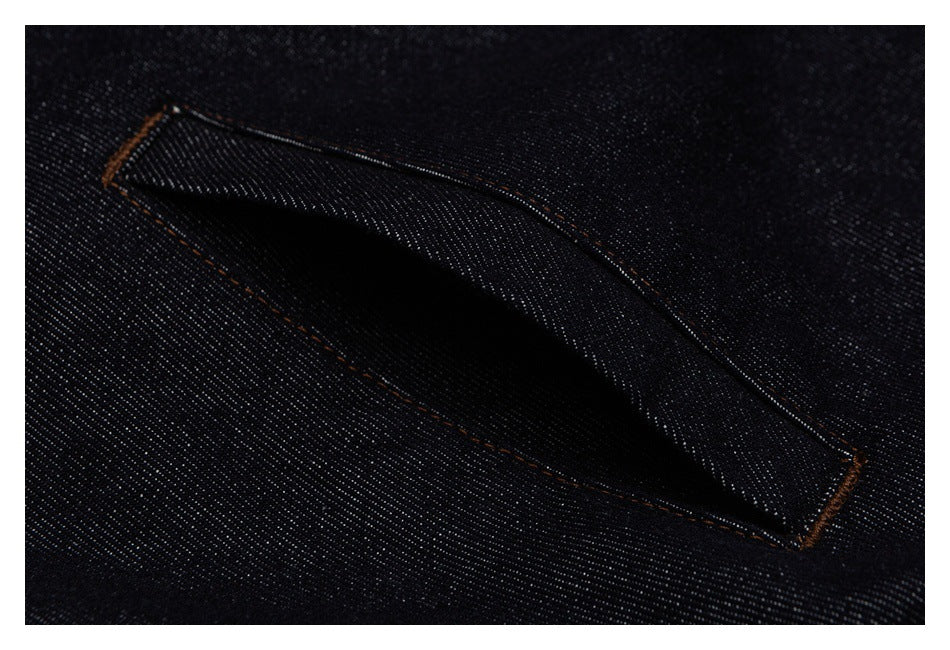 Close-up of an angled welt pocket on dark indigo denim, edged with contrasting orange stitching.
