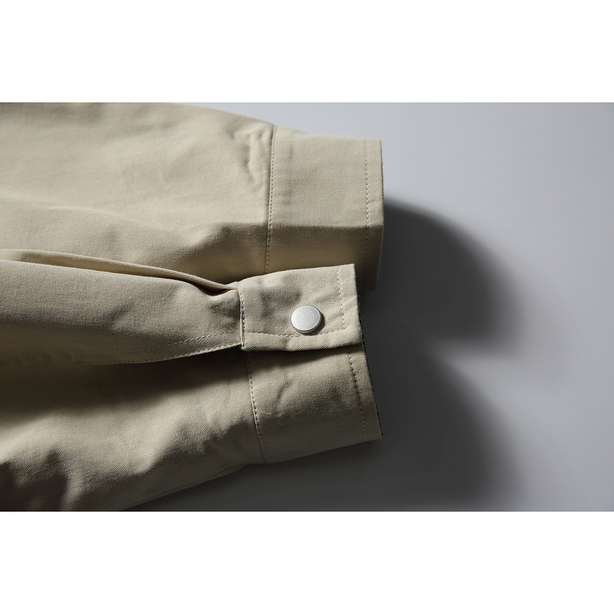 Close-up of a beige jacket sleeve cuff with a silver snap tab and visible stitching.