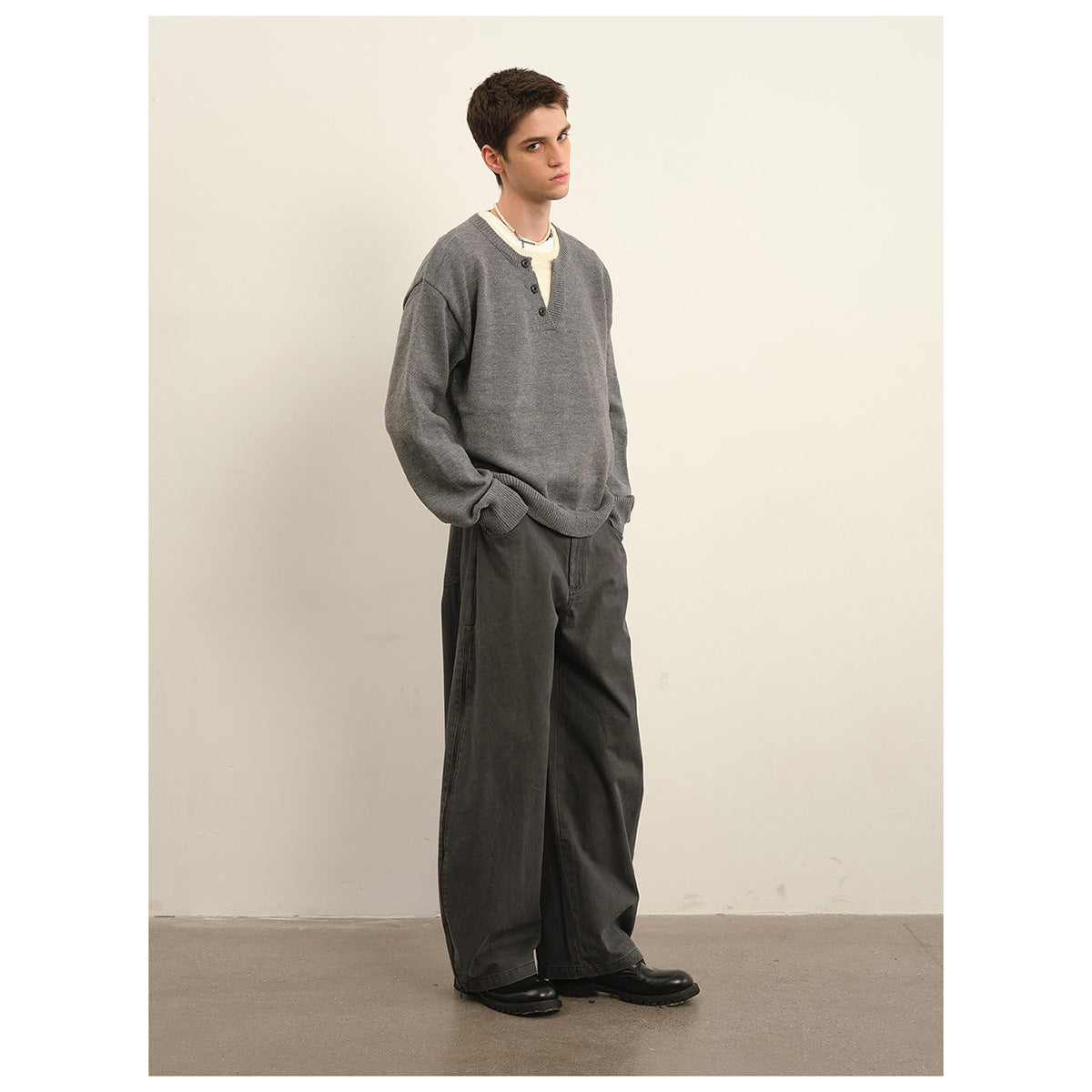 Model wearing a gray long-sleeve sweater with a three-button split neckline and ribbed cuffs, styled with wide dark pants.