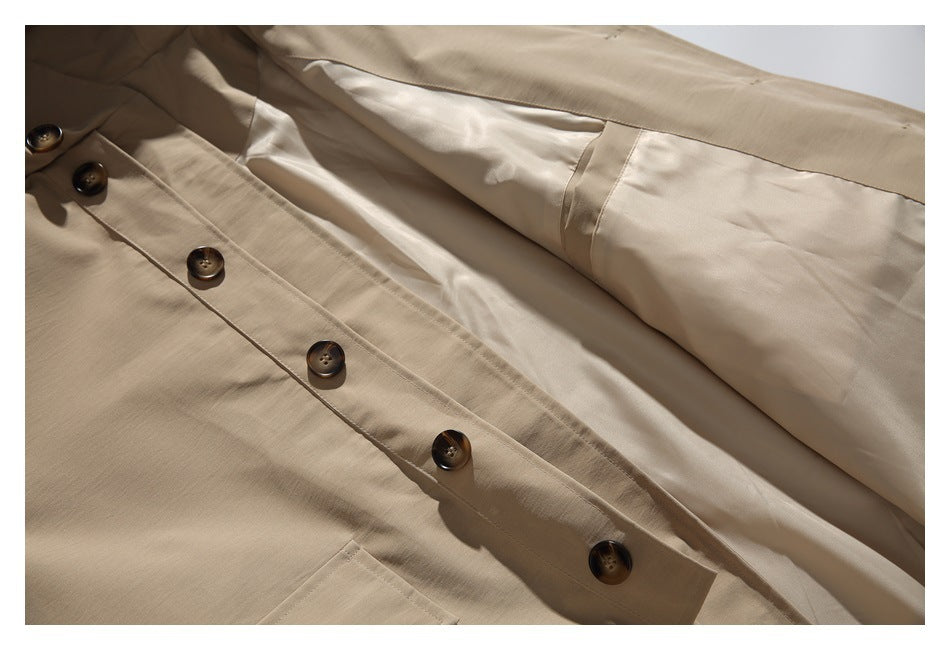 Close-up of an open beige coat showing its dark-button front placket and light lining.