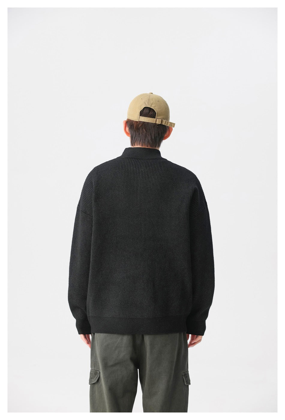 Back view of a model wearing a black ribbed sweater with a high collar and dark gray trousers.