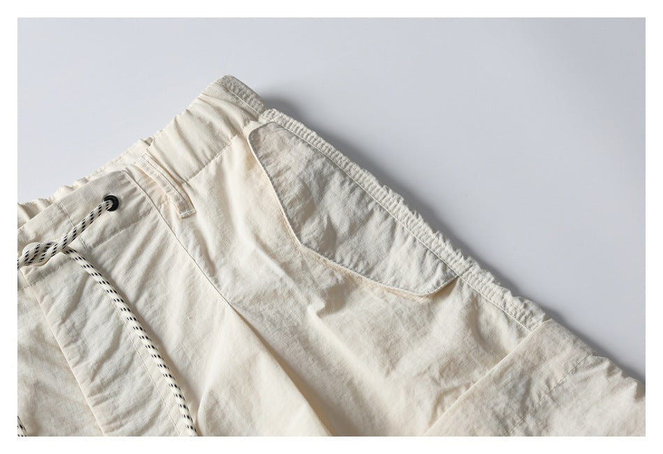 Close-up of off-white shorts showing a side pocket, elastic waistband, belt loop and black-and-white drawcord.