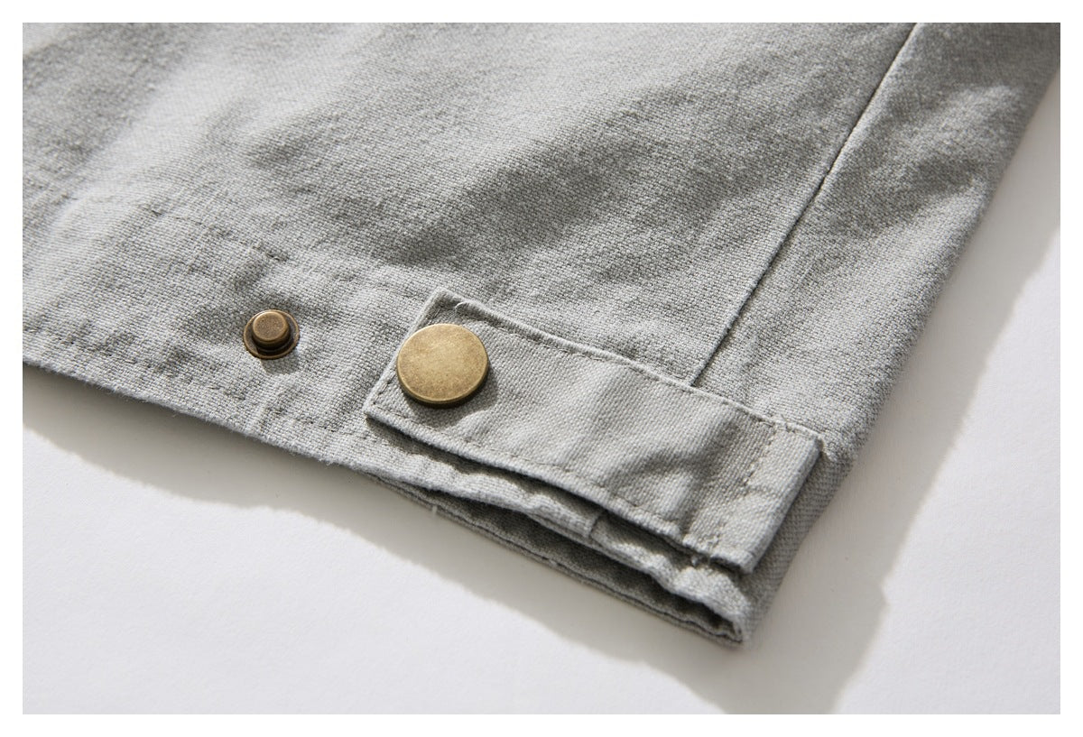 Close-up of a light gray jacket cuff with an adjustable tab and brass snap fasteners.