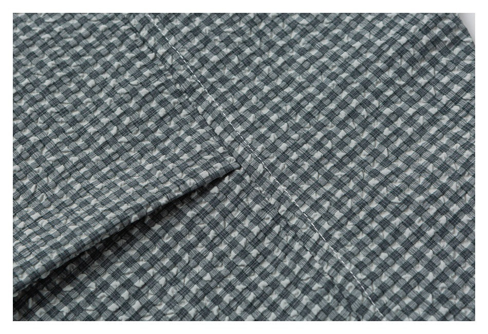 Close-up of gray check shirt fabric with a folded edge and visible seam stitching.
