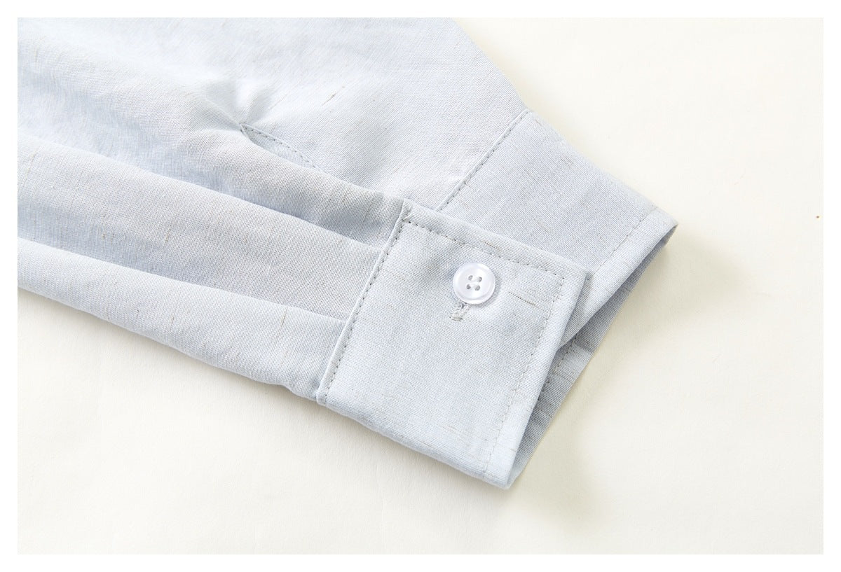 Close-up of a pale blue-gray shirt sleeve cuff with a white button and visible stitching.