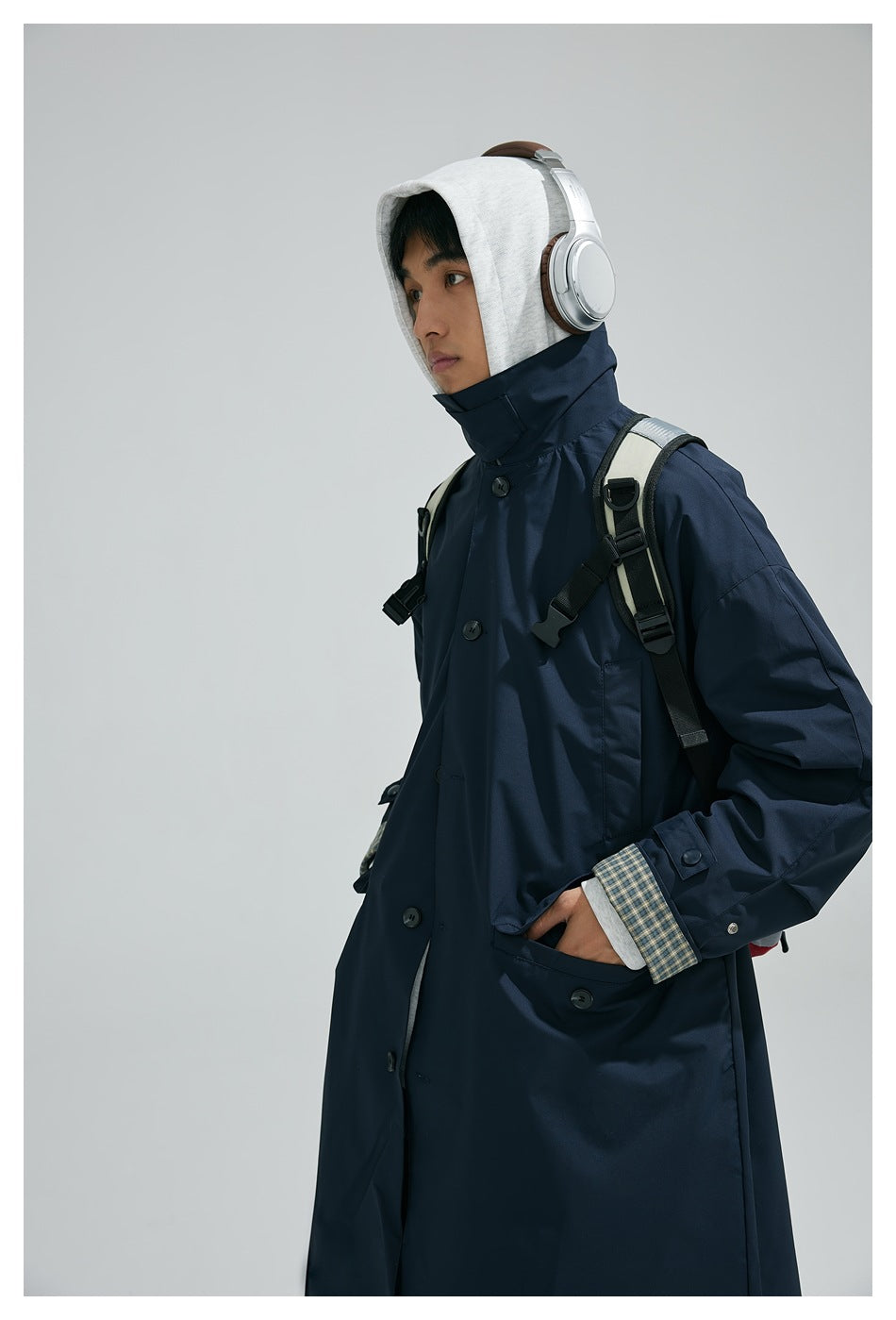 Person wearing a navy long coat with a high collar, checked cuffs, and large pockets.