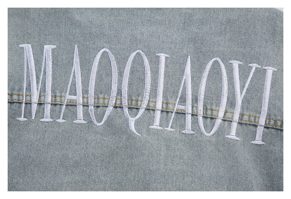 Close-up of large white embroidered lettering across the back of a light blue denim jacket.