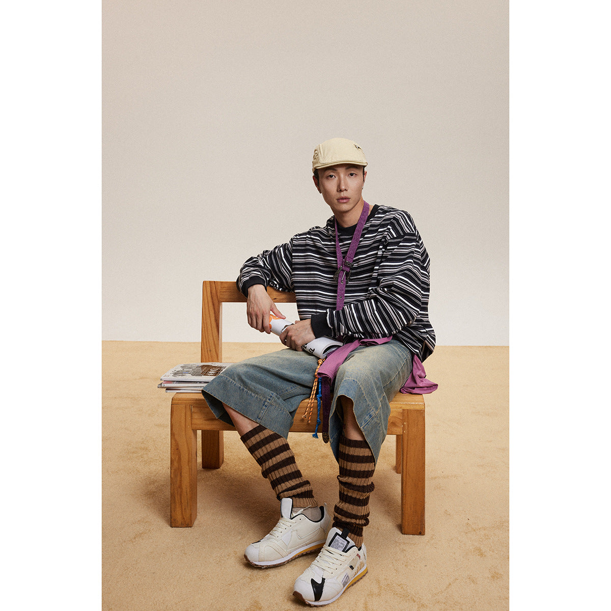 Model seated in a black-and-white striped long-sleeve shirt, denim shorts, striped leg warmers and sneakers.