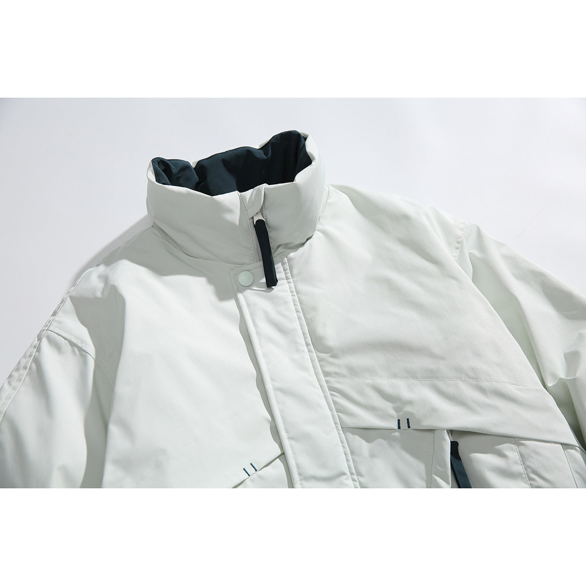 Close-up of a white jacket's high collar, dark lining, front placket and black pull tab.