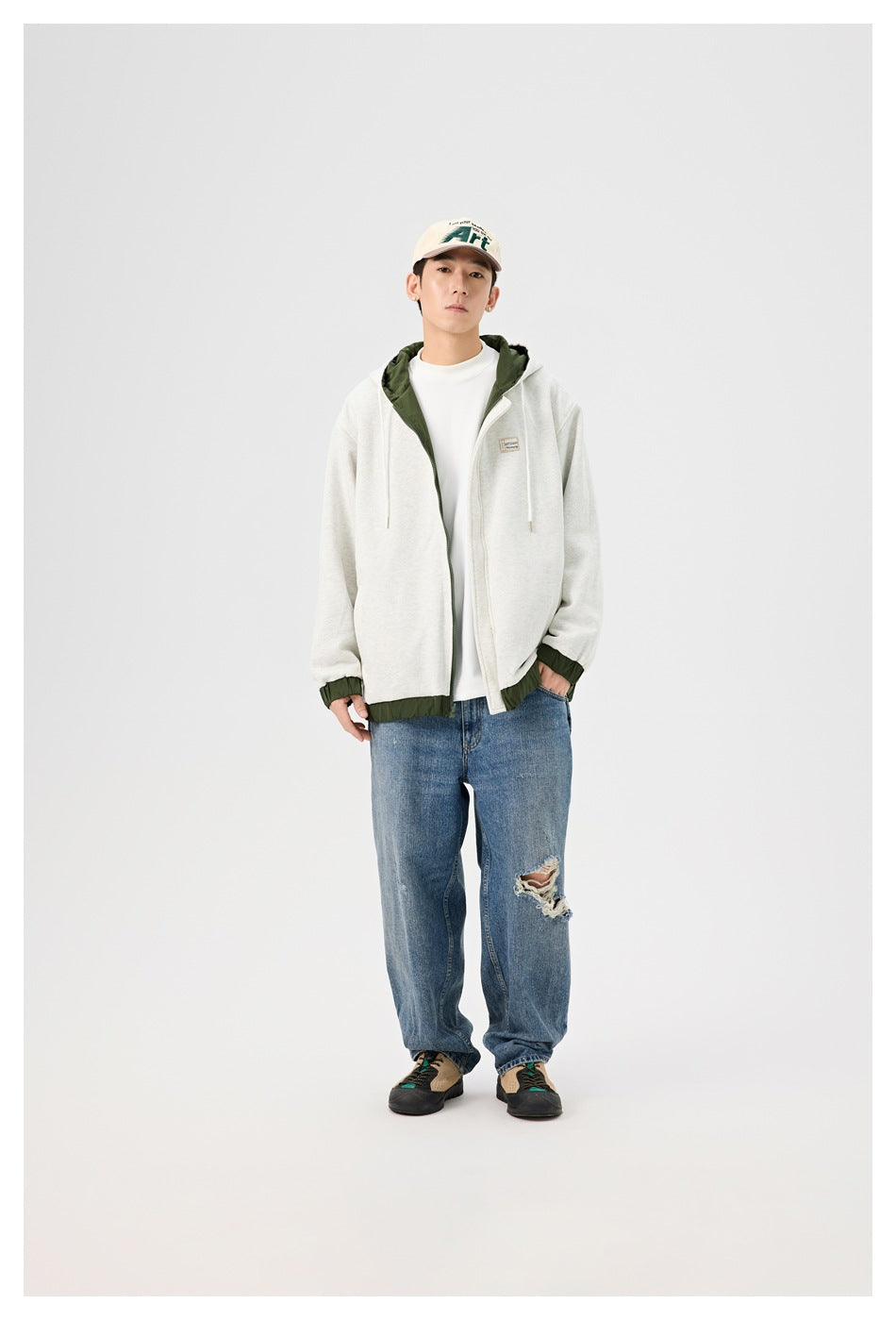 Full-length model wearing a light gray hooded zip jacket with dark green accents and loose distressed blue jeans.