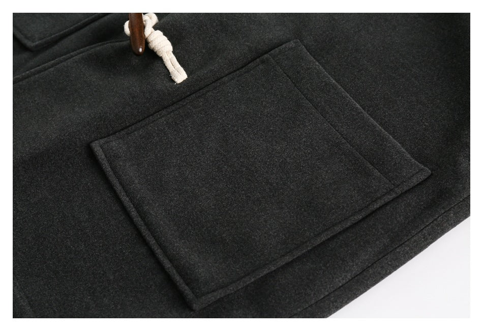 Close-up of a charcoal coat's large rectangular patch pocket and cream rope toggle fastening.