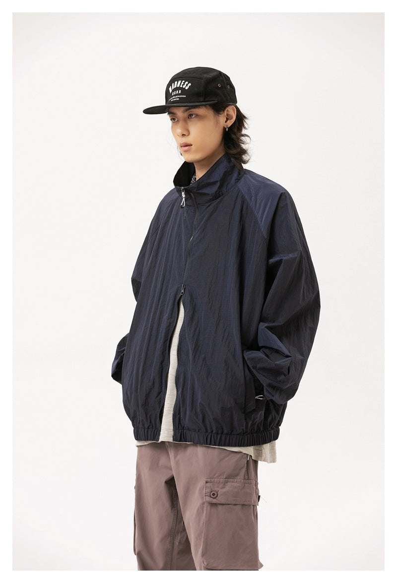 Model wearing a dark navy zip-front jacket with a raised collar and elastic hem, styled with a black cap and mauve cargo