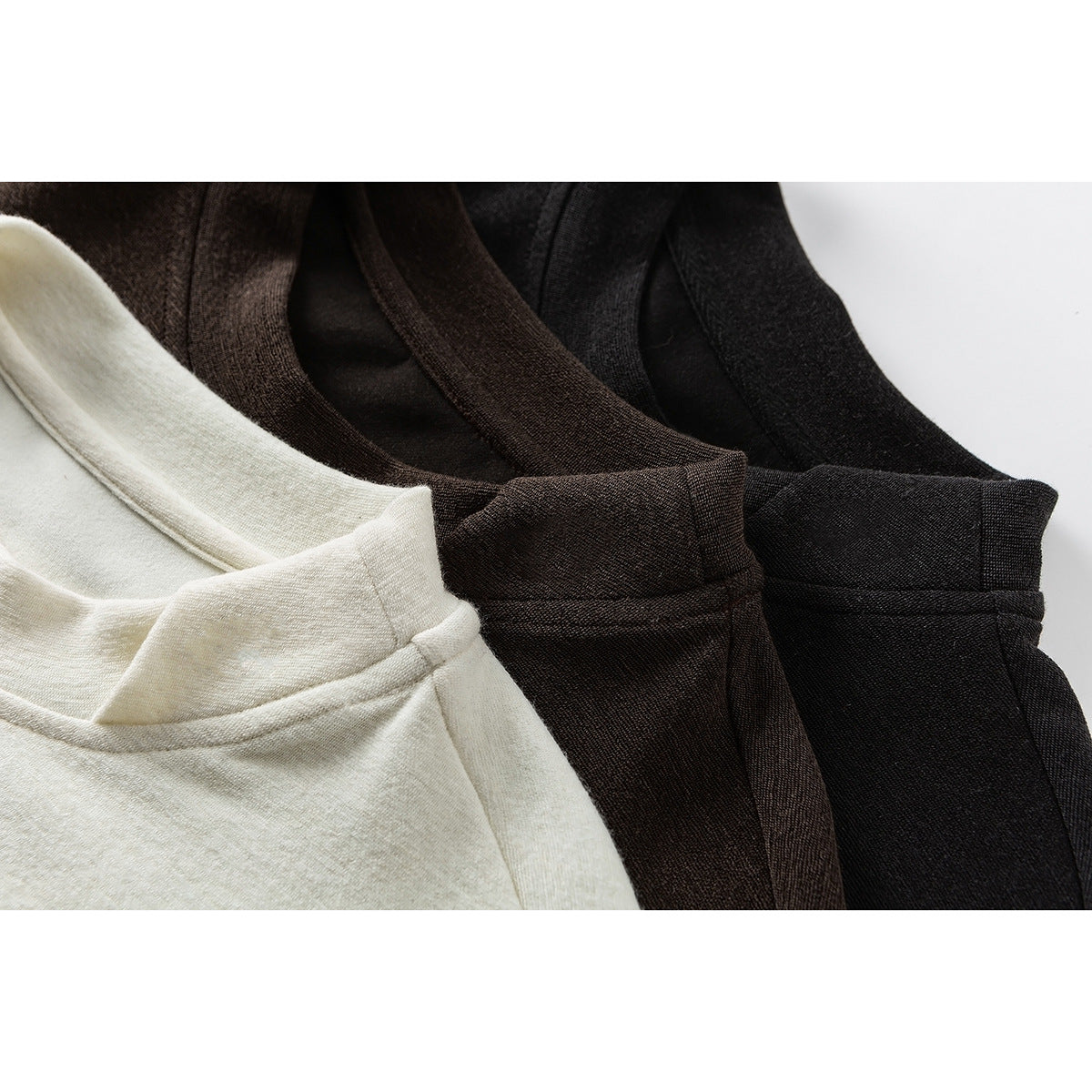 Close-up of three overlapping shirt necklines in ivory, dark brown, and black.